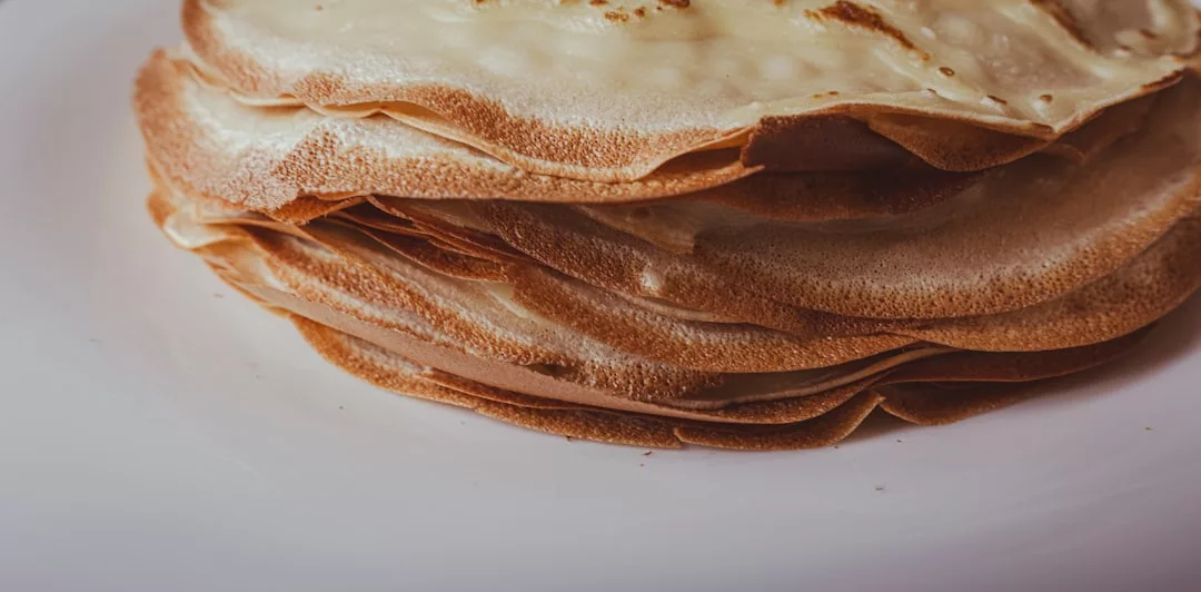 Eine Nahaufnahme eines Stapels dünner, goldbrauner Crêpes auf einem weißen Teller, der an die köstlichen Frühstücksleckereien auf Mallorca erinnert.