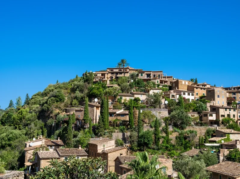 Das Bergdorf Deià mit Kirche auf dem Hügel und Steinhäusern zwischen Zypressen in der Tramuntana