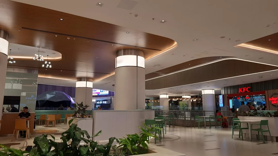 Geräumiger Food-Court-Bereich in einem Einkaufszentrum auf Mallorca mit moderner Beleuchtung, grünen Sitzgelegenheiten, Zimmerpflanzen und einer sichtbaren KFC-Filiale im Hintergrund.