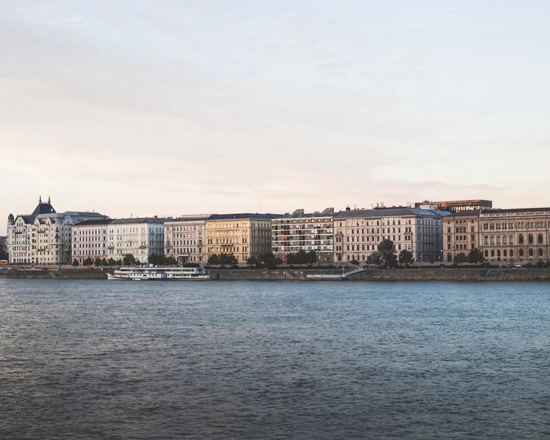 Eine Reihe historischer Gebäude säumt die Uferpromenade unter einem blassen Himmel auf Mallorca. Im Vordergrund fährt ein weißes Flussschiff über das Wasser.