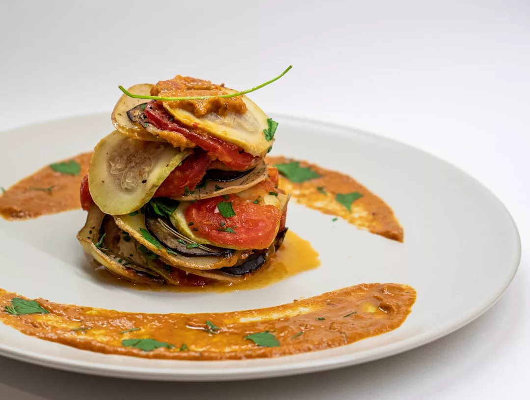 Eine ordentlich gestapelte Portion Ratatouille mit geschnittenem Gemüse und Tomatensauce, garniert mit frischen Kräutern auf einem weißen Teller, inspiriert von den lebhaften Aromen Mallorcas.