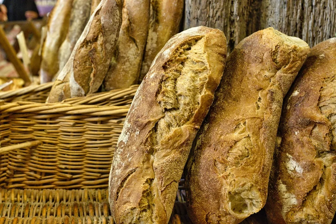 Mehrere rustikale Brotlaibe, die von der traditionellen mallorquinischen Backkunst inspiriert sind, werden aufrecht neben einem geflochtenen Korb und einer Weidenfläche präsentiert.