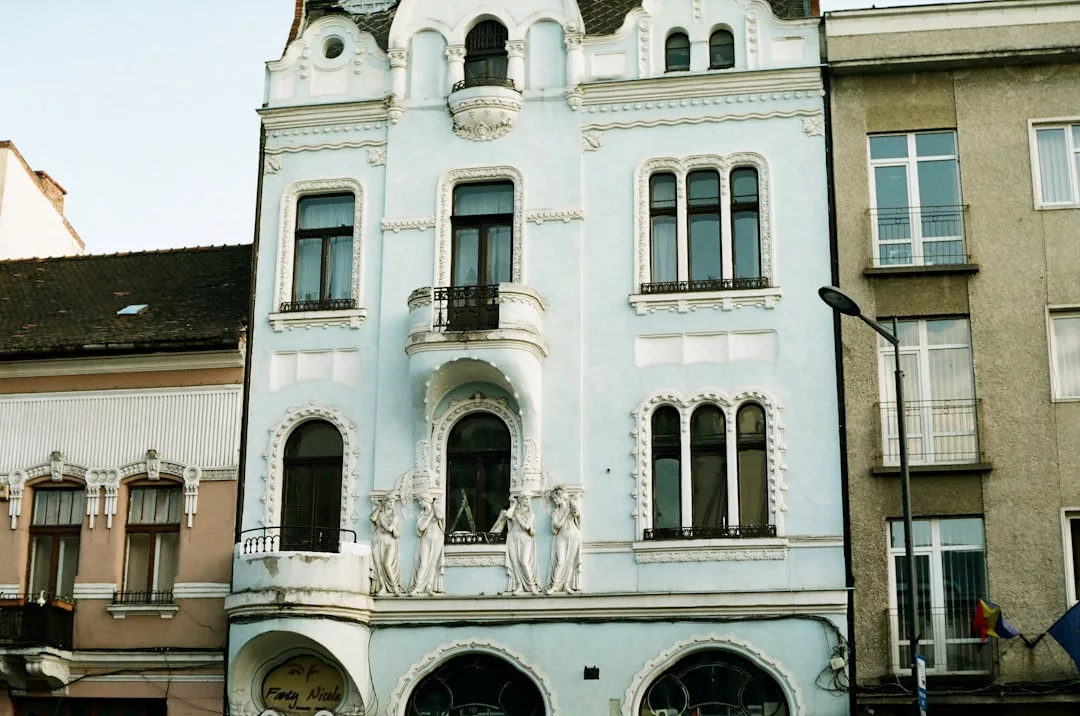 Ein hellblaues, dreistöckiges historisches Gebäude mit verschnörkelten architektonischen Details und geschnitzten Figuren an der Fassade, das an die charmante Architektur Mallorcas erinnert und zwischen zwei anderen Gebäuden liegt.
