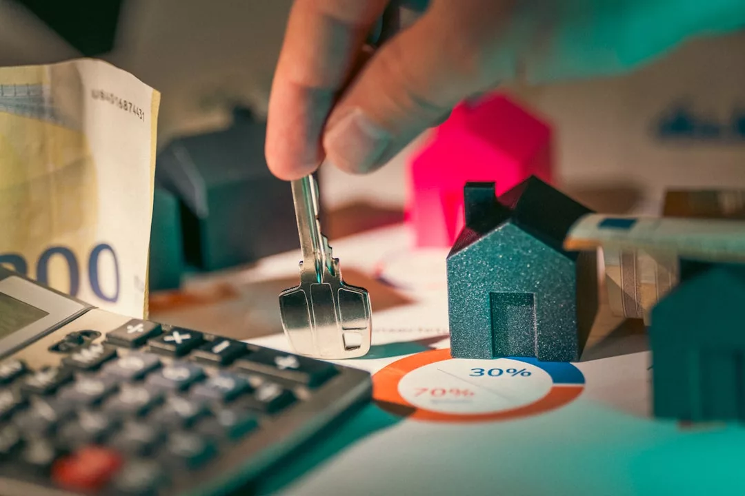 Eine Hand hält Hausschlüssel in der Nähe von Miniaturhäusern, einen Taschenrechner, Euro-Scheine und ein Tortendiagramm, was auf Finanzplanung oder Immobilieninvestitionen auf Mallorca hindeutet.