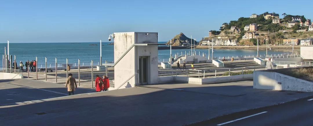 Eine Küstenpromenade auf Mallorca mit spazierenden Menschen, weißen Geländern und Gebäuden auf einem Hügel am Meer unter einem klaren blauen Himmel.