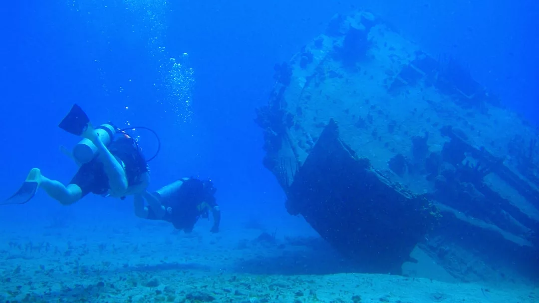 Zwei Taucher erkunden ein Schiffswrack, das in der Nähe von Mallorca auf dem Meeresgrund liegt, umgeben von blauem Wasser und Luftblasen.