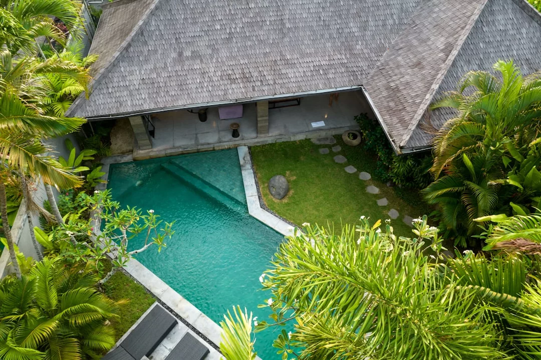 Luftaufnahme eines Hauses auf Mallorca mit Strohdach, privatem Swimmingpool, Sonnenliegen und üppigen tropischen Pflanzen und Bäumen.