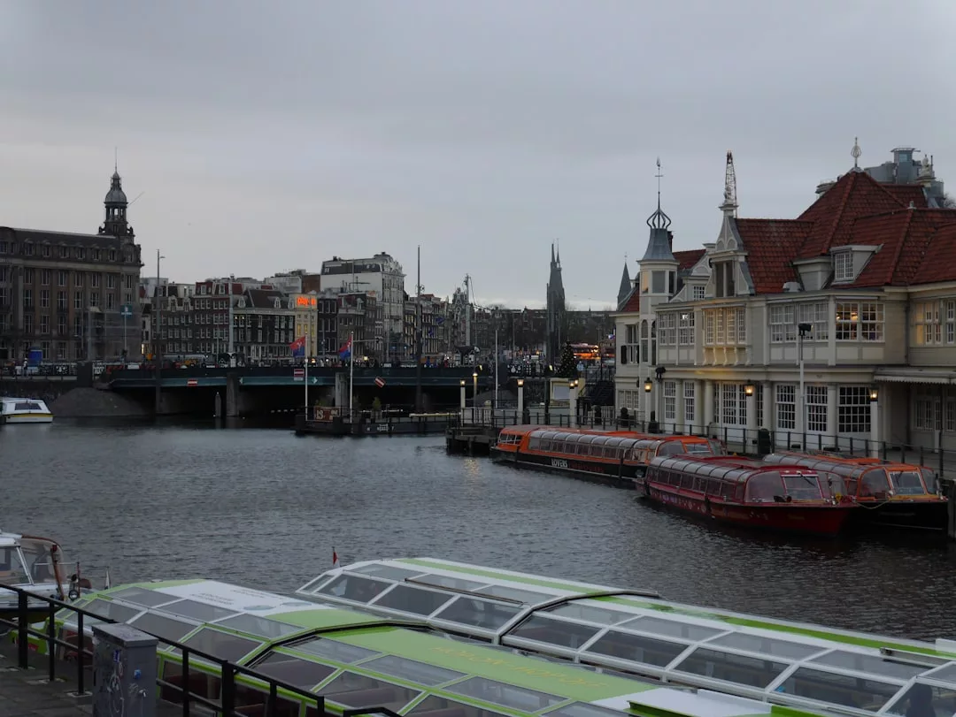 Ein bewölkter Tag in Amsterdam mit angedockten Booten an einer Gracht, historischen Gebäuden im Hintergrund und einer Brücke, die über das Wasser führt, weckt Erinnerungen an Mallorcas malerische Uferpromenaden und europäischen Charme.