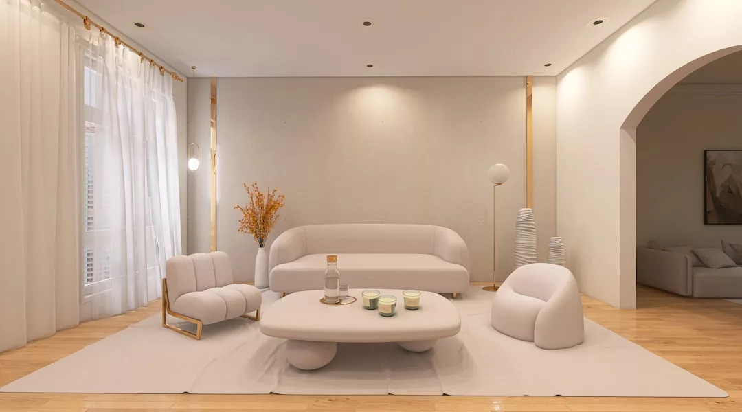 Ein minimalistisches, von Mallorca inspiriertes Wohnzimmer mit weißen Möbeln, einem niedrigen Couchtisch mit Kerzen und einer Flasche, hellen Holzböden und durchsichtigen Vorhängen, die das natürliche Licht hereinlassen.