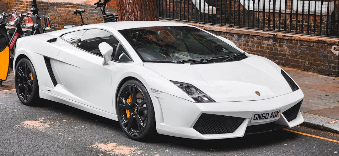 Ein weißer Lamborghini-Sportwagen parkt auf einer Stadtstraße auf Mallorca, neben einem Bürgersteig und einer Backsteinmauer.