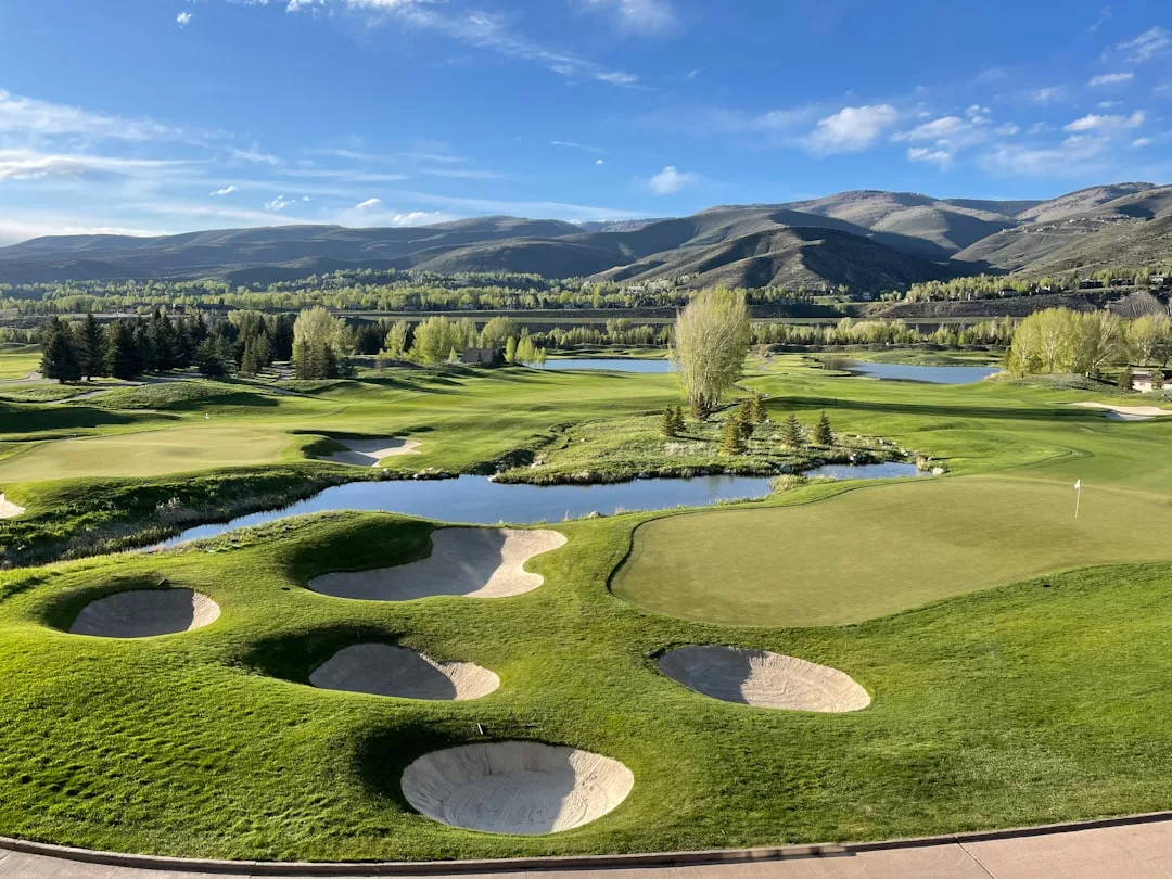 Ein mallorquinischer Golfplatz mit mehreren Sandbunkern, einem üppigen Grün, Wasserspielen und Bäumen, alles eingebettet in sanfte Hügel und einen teilweise bewölkten Himmel.