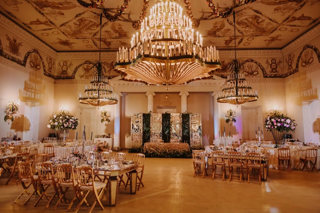 Eleganter Ballsaal mit verschnörkelten Kronleuchtern, dekorierten Tischen, Blumenarrangements und einer Blumenbühne, die den Charme Mallorcas versprüht und für eine formelle Veranstaltung oder einen Hochzeitsempfang eingerichtet wurde.
