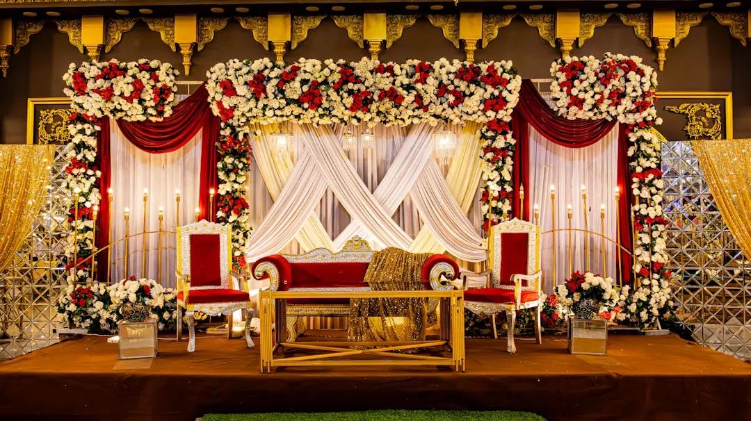 Eine dekorierte Hochzeitsbühne auf Mallorca mit roten und goldenen Stühlen, einem passenden Sofa, Blumenarrangements, drapierten Stoffen und goldenen Akzenten.
