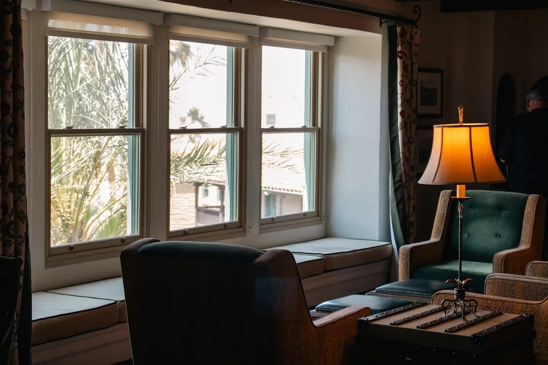 Ein gemütliches Wohnzimmer mit zwei Sesseln, einer Lampe und einem Fensterplatz neben großen Fenstern mit Blick auf Mallorcas ikonische Palmen draußen.