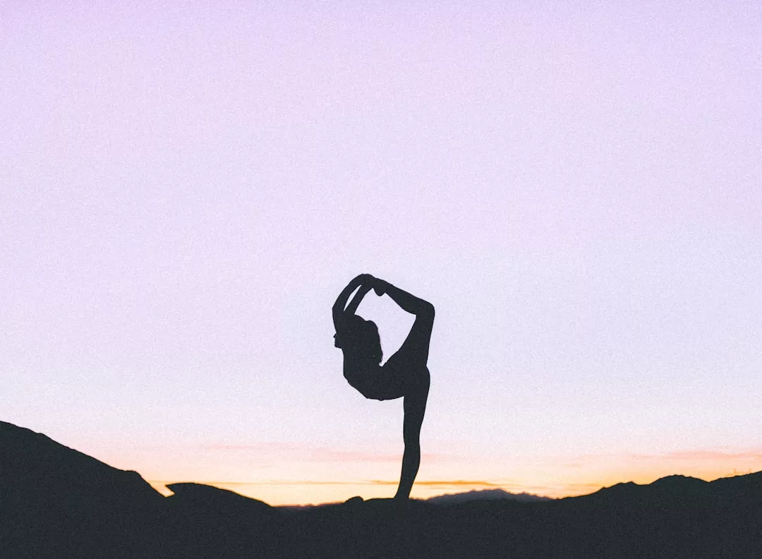 Silhouette einer Person, die eine stehende Yoga-Pose im Freien bei Sonnenuntergang auf Mallorca ausführt, mit einem klaren Himmel im Hintergrund.