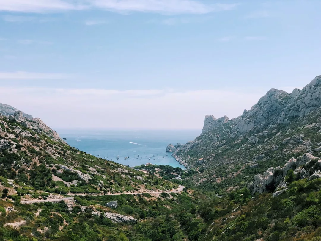 Blick auf eine Küstenbucht auf Mallorca, umgeben von felsigen Hügeln, mit Booten, die im blauen Wasser ankern, und spärlicher Vegetation, die die Landschaft unter einem klaren Himmel bedeckt.