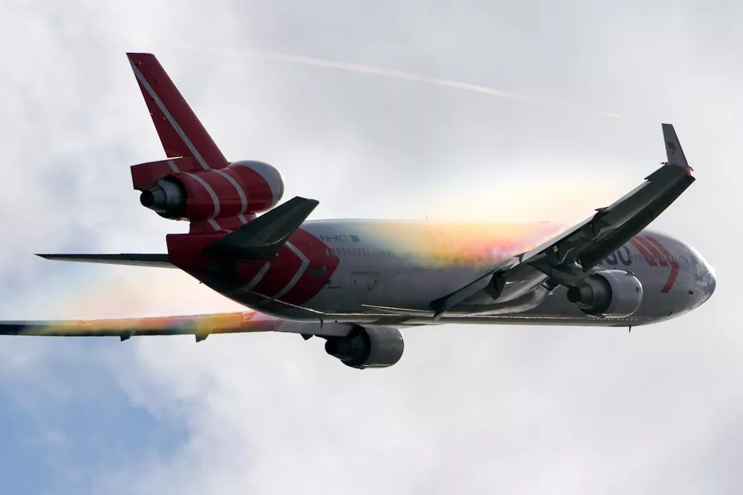 Ein großes Düsenflugzeug im Flug, von unten betrachtet, erzeugt einen regenbogenfarbenen Dampfeffekt in der Nähe seiner Tragflächen vor einem bewölkten Himmel über Mallorca.
