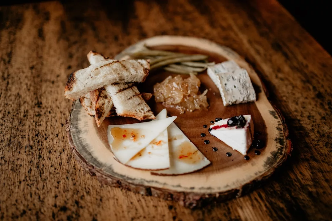 Eine Holzplatte mit getoasteten Brotscheiben, drei Käsesorten, eingelegten grünen Bohnen, Obstkonserven und ein paar Brombeeren auf einem rustikalen Holztisch auf Mallorca.