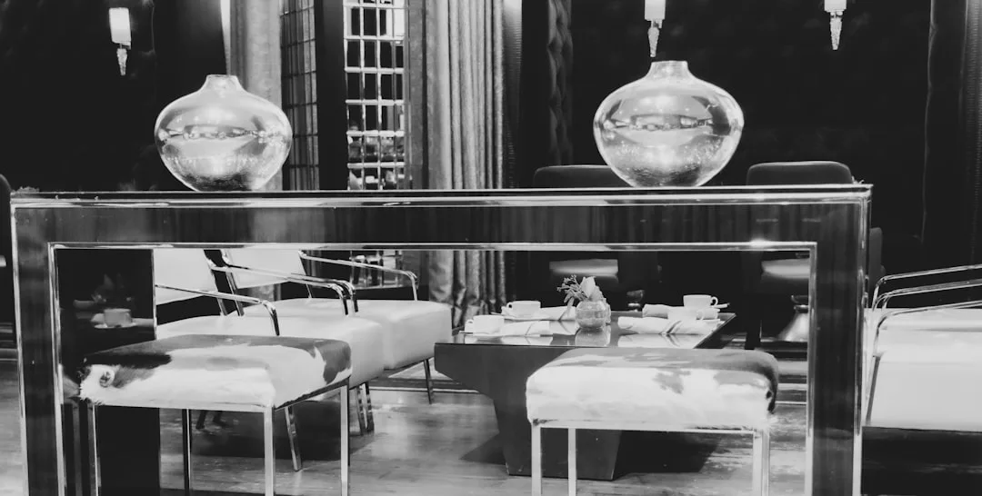Schwarz-Weiß-Foto einer modernen Mallorca-Lounge mit Hockern aus Kuhfell, einem Spiegeltisch mit zwei Glasvasen, Sesseln und einem Couchtisch mit Tassen und Untertassen.