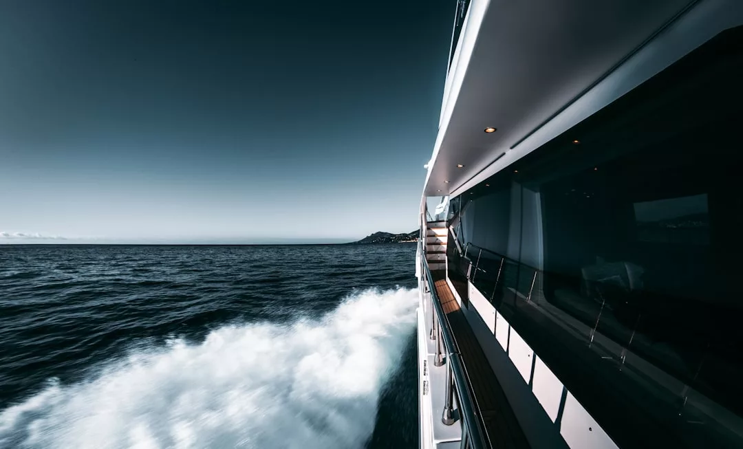 Blick von der Seite einer fahrenden Yacht in der Nähe von Mallorca, mit Blick auf das Meer, die ferne Küste und das Kielwasser hinter dem Boot bei klarem Himmel.