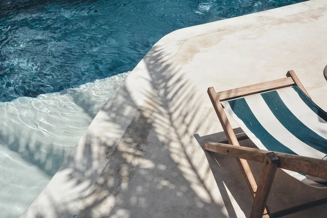 Ein gestreifter Liegestuhl steht auf einem Betonpool neben dem klaren blauen Wasser, und die Schatten der Palmen auf der Oberfläche erinnern an den entspannten Charme von Mallorca.