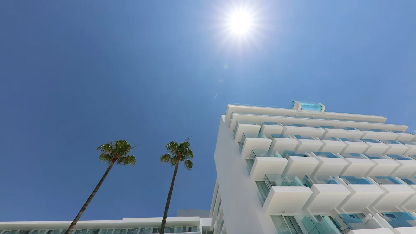 Weiße Fassade des Iberostar Waves Bahía de Palma mit Palmen unter blauem Himmel