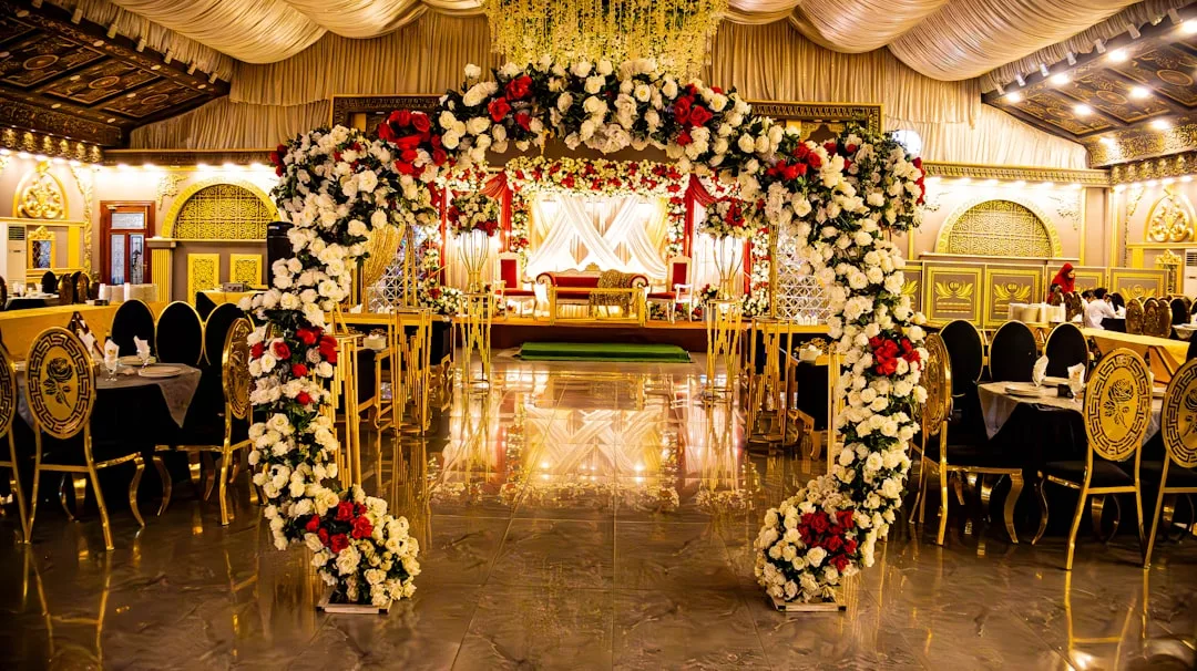 Ein geschmückter Bankettsaal auf Mallorca mit einem Bogengang aus weißen und roten Blumen, goldenen und schwarzen Stühlen und einer Bühne mit einem Sofa im Hintergrund.