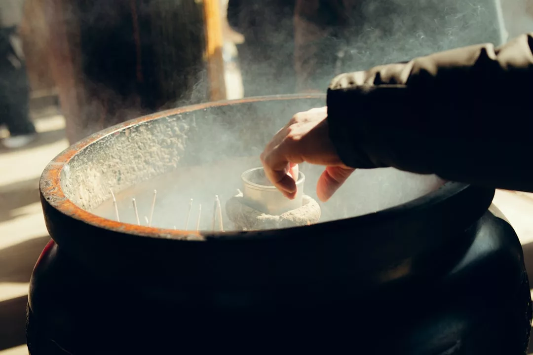Eine Hand streckt sich über ein großes, mit Rauch gefülltes Räuchergefäß, in dem sich Räucherstäbchen und eine Opferschale befinden - eine heitere rituelle Szene, inspiriert vom ruhigen Geist Mallorcas.