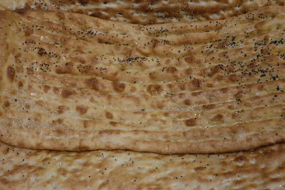 Nahaufnahme eines rechteckigen mallorquinischen Fladenbrots mit geriffelten Linien und mit schwarzem Sesam oder Mohn bestreut.