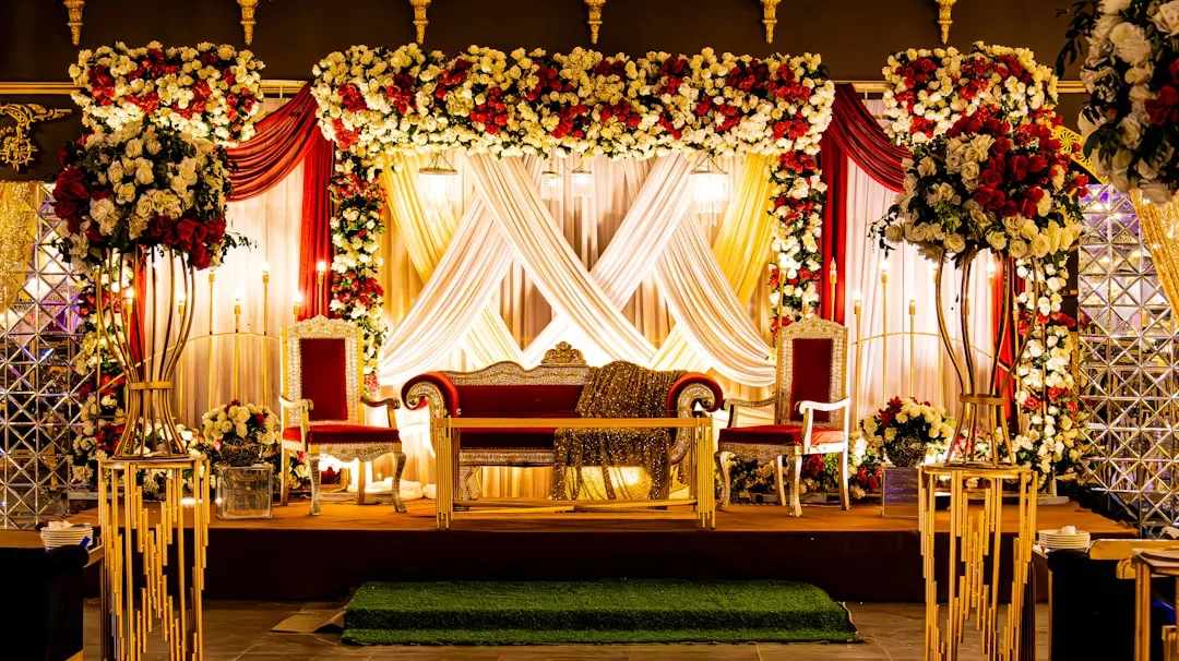 Eine dekorierte Hochzeitsbühne auf Mallorca mit einem rot-weißen Blumenbogen, drapierten weißen Vorhängen, verzierten Stühlen und goldenen Kerzenhaltern.