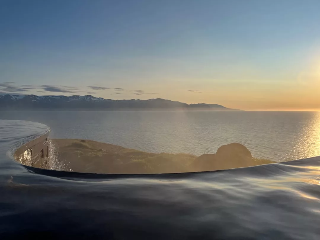 Infinity-Pool im Vordergrund mit ruhigem Wasser, mit Blick auf das glitzernde Wasser Mallorcas und die fernen Berge bei Sonnenuntergang.