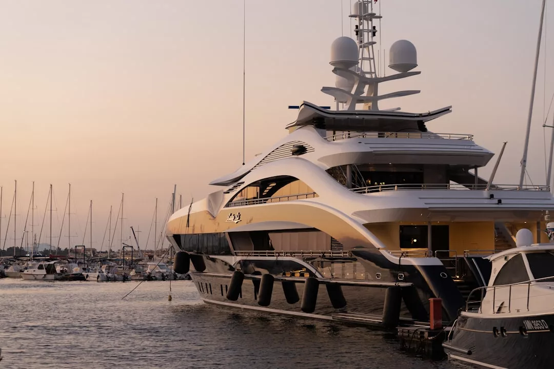 Eine große Luxusyacht liegt bei Sonnenuntergang in einem mallorquinischen Yachthafen vor Anker, umgeben von kleineren Booten und Segelschiffen.