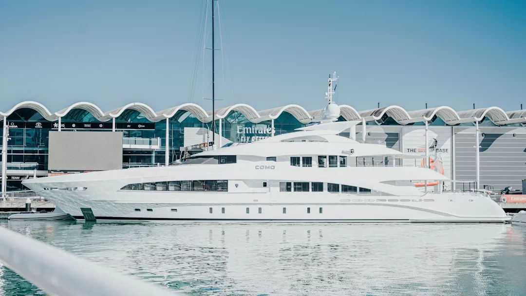 Eine große weiße Yacht mit dem Namen COMO liegt in einem Yachthafen auf Mallorca vor einem modernen Gebäude und ruhigem Wasser im Hintergrund unter einem strahlend blauen Himmel.