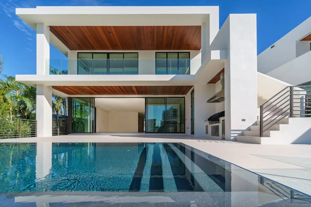 Modernes zweistöckiges Haus mit großen Glasfenstern, hölzernen Deckenakzenten, einem Balkon und einem Swimmingpool im Vordergrund - perfekt, um Mallorcas klaren blauen Himmel zu genießen.