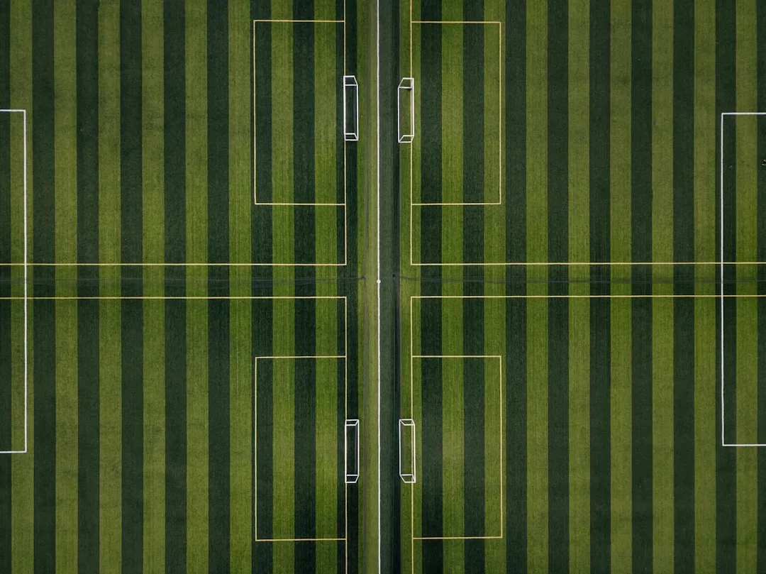 Luftaufnahme eines Fußballplatzes auf Mallorca mit abwechselnd hell- und dunkelgrünen Streifen, Linien, die vier Tore markieren, und einer zentralen Trennlinie.