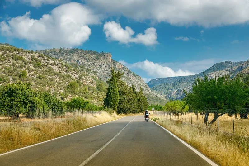 Motorradfahrer auf einer Landstraße vor den Kalkfelsen der Serra de Tramuntana auf Mallorca