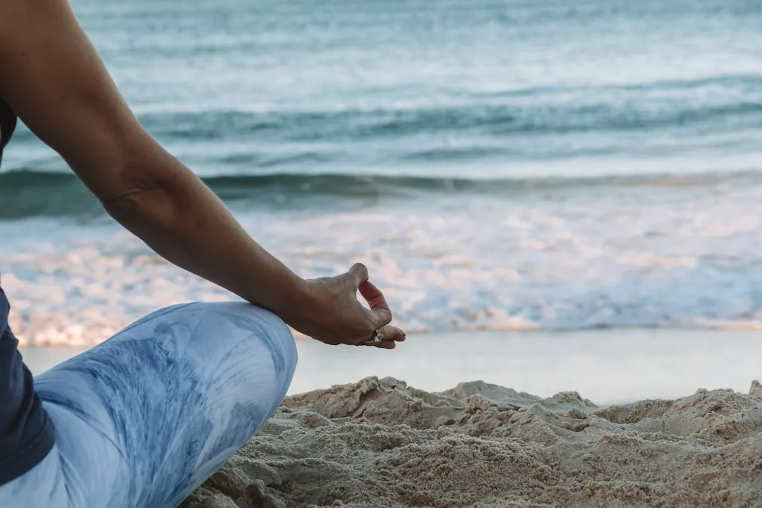 Person im Schneidersitz am Sandstrand von Mallorca, die Hände in Meditationshaltung auf die Knie gestützt, mit Blick auf die sanften Wellen des Meeres.