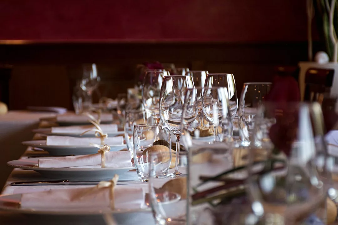 Ein langer Esstisch ist mit weißen Servietten, Tellern, Besteck und mehreren Gläsern für ein formelles Essen in einem schwach beleuchteten Restaurant auf Mallorca gedeckt.