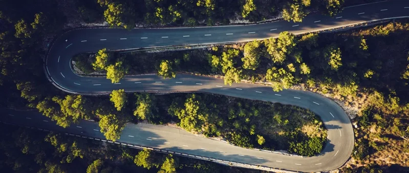 Serpentinen einer Bergstraße zwischen Pinien in der Serra de Tramuntana aus der Luft