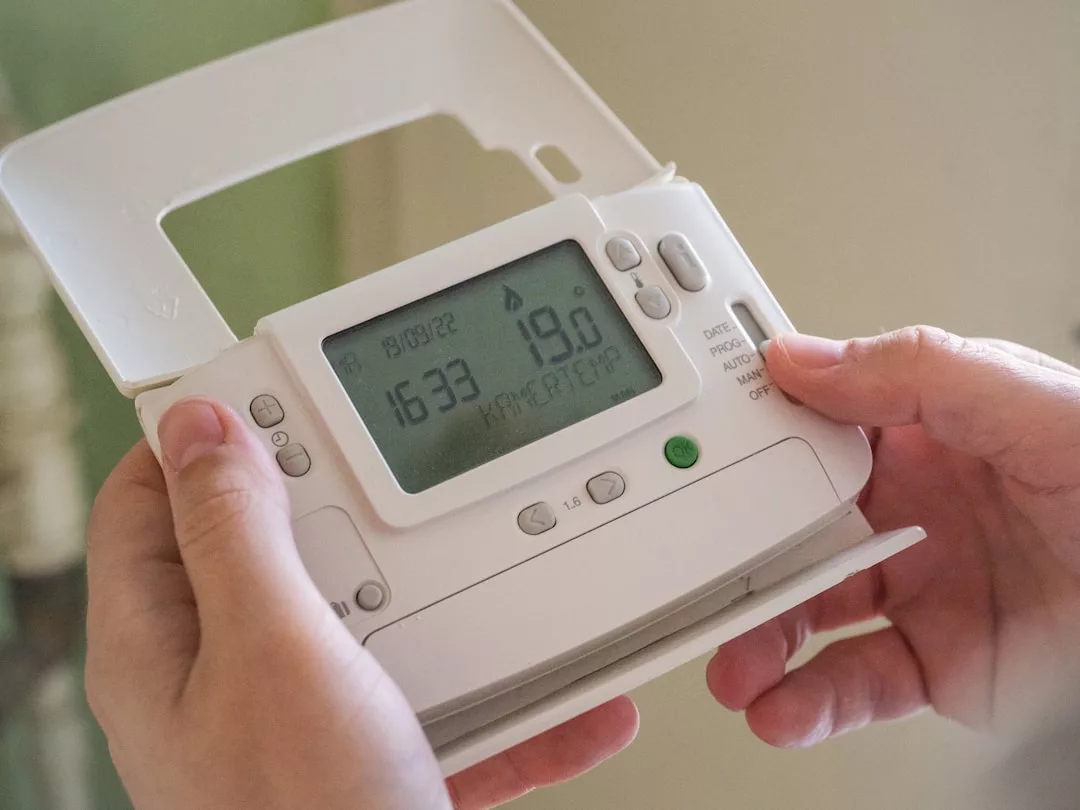 Eine Person auf Mallorca stellt ein digitales Thermostat ein, das die Temperatur, die Uhrzeit und das Datum anzeigt, wobei mehrere Tasten sichtbar sind.
