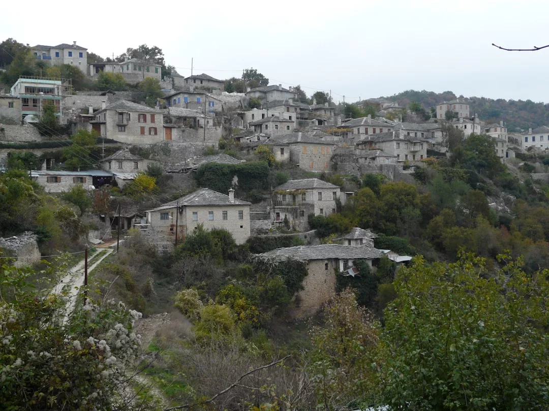 Hügeliges Dorf mit Steinhäusern auf Mallorca, umgeben von Bäumen und Vegetation unter einem bedeckten Himmel.