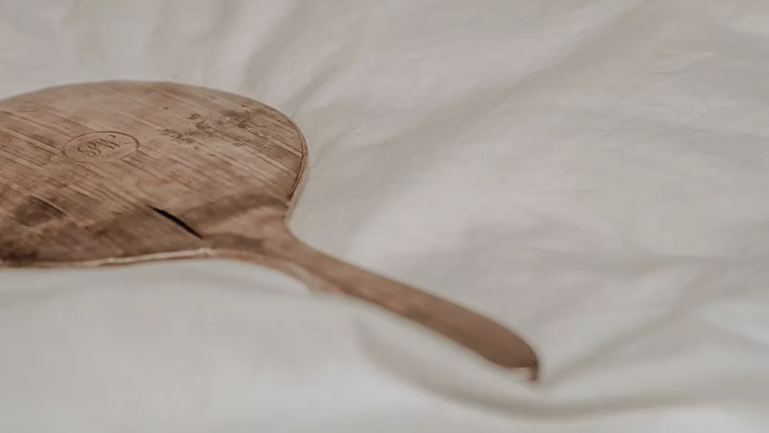 Ein abgenutztes Holzpaddel mit rissiger Oberfläche, das an den Küstencharme Mallorcas erinnert, ruht auf einem weißen Stoffhintergrund.