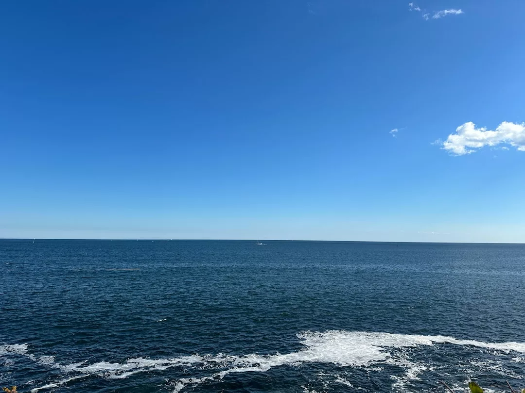 Ein ruhiges Meer unter einem klaren blauen Himmel mit ein paar Wolken und sanften Wellen in Ufernähe, die an die ruhige Schönheit Mallorcas erinnern.