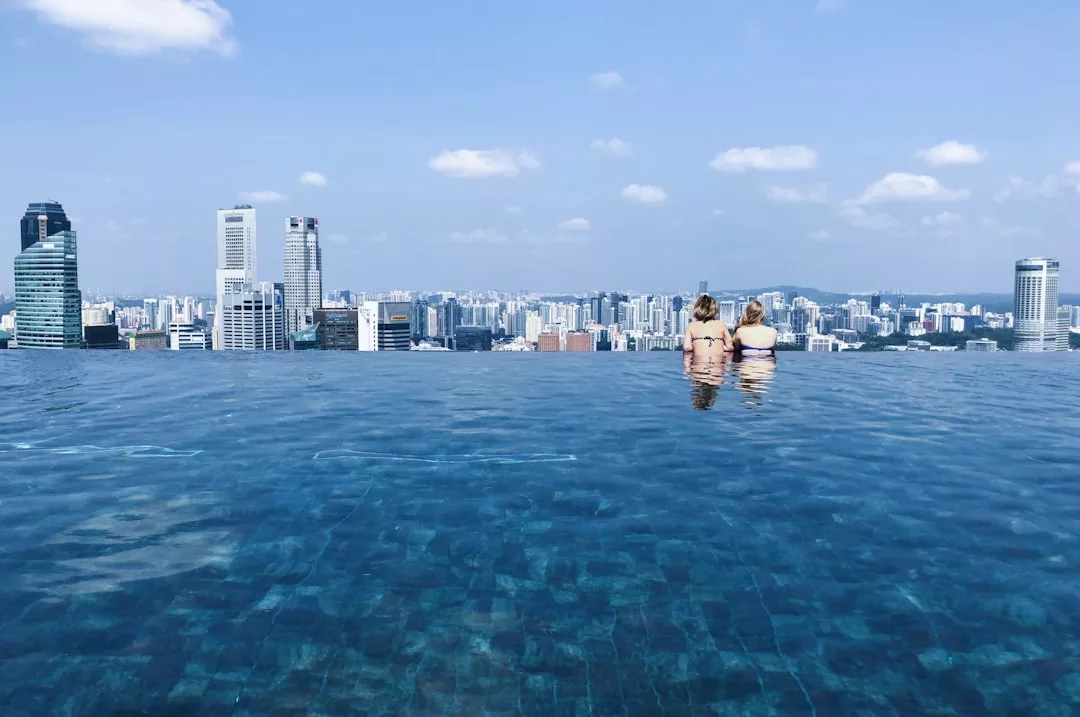 Zwei Menschen stehen in einem Infinity-Pool und blicken auf die Skyline der Stadt, während die Schönheit Mallorcas unter einem klaren blauen Himmel mit vereinzelten Wolken leuchtet.