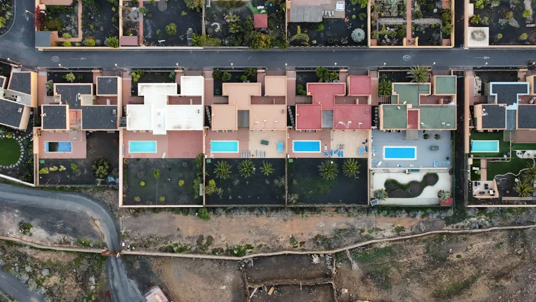 Luftaufnahme einer Reihe moderner Häuser mit Flachdächern und Swimmingpools auf Mallorca, getrennt durch Zäune, umgeben von Straßen und angelegten Gärten.