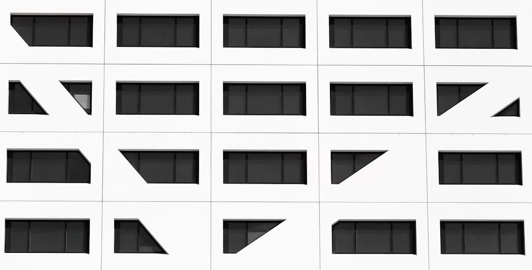 Eine weiße Gebäudefassade auf Mallorca weist mehrere Reihen rechteckiger Fenster auf, von denen einige von diagonalen weißen Paneelen eingerahmt sind, die ein auffälliges geometrisches Muster bilden.
