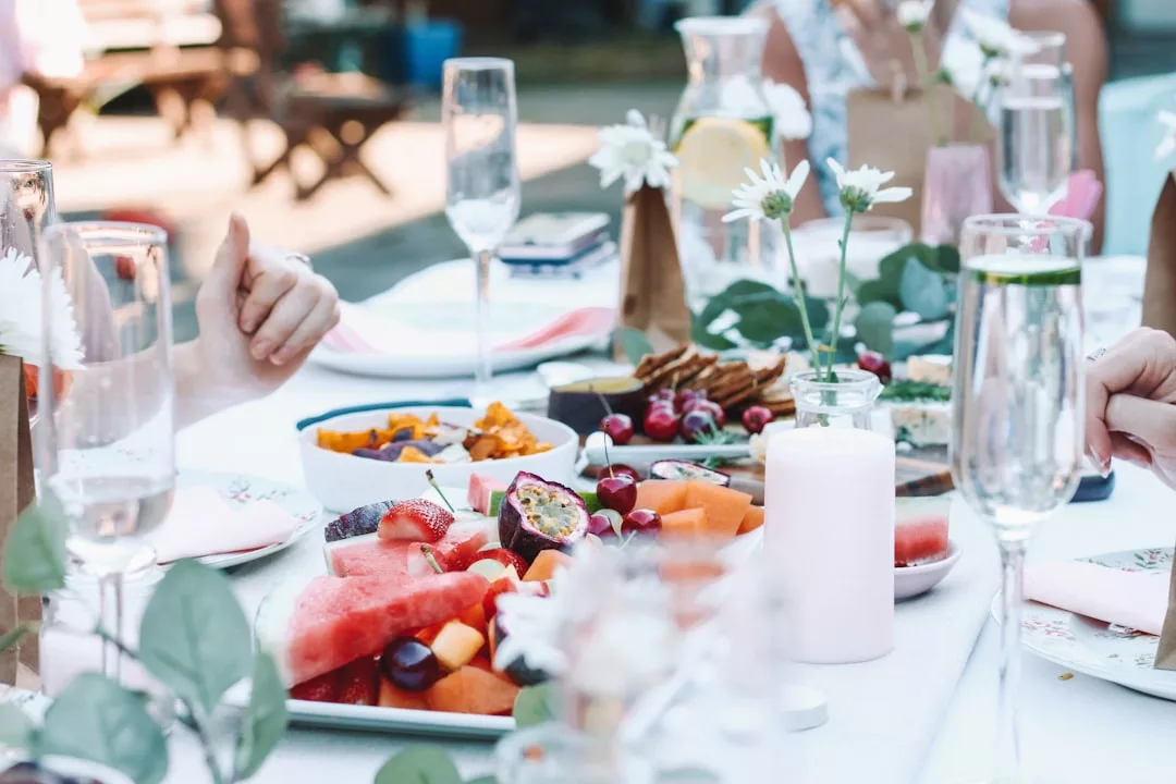 Ein im Freien gedeckter Tisch auf Mallorca mit verschiedenen frischen Früchten, Crackern und Käse, umgeben von Gläsern mit prickelnden Getränken, Kerzen und Blumendekorationen.
